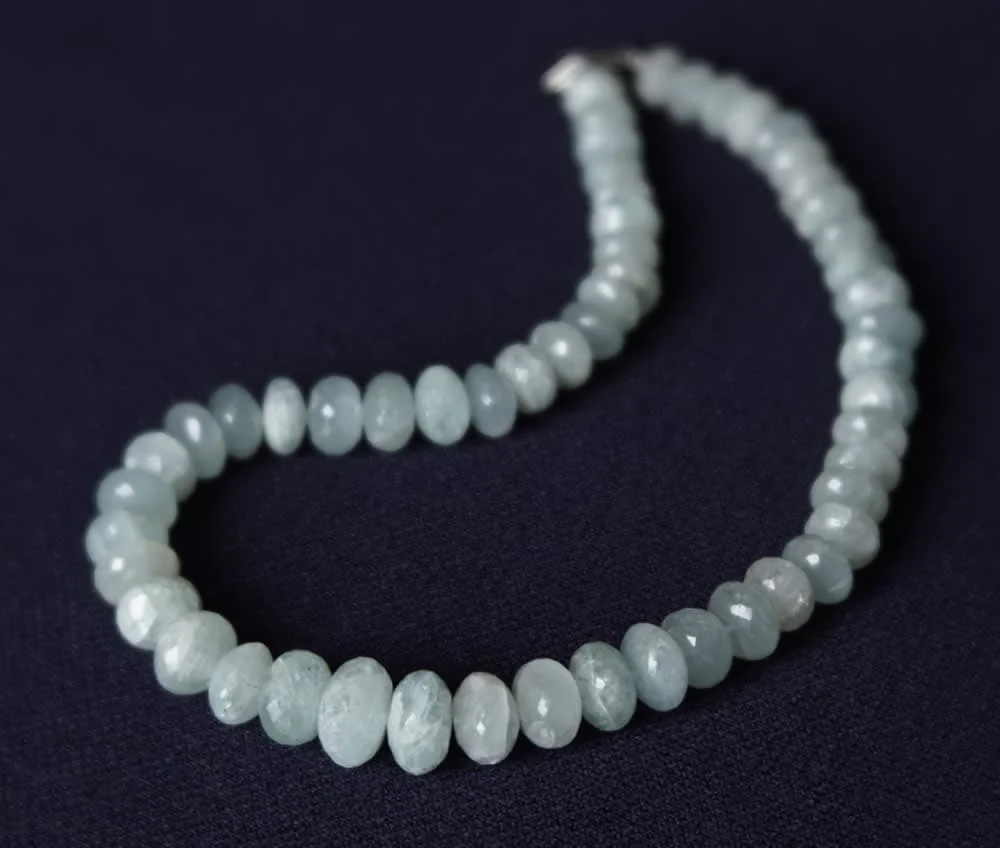 Un Collier de pierres facettes d'aigue-marine brutes avec des perles de jade blanc sur fond noir, orné de pierres précieuses facettées d'aigue-marine brute.