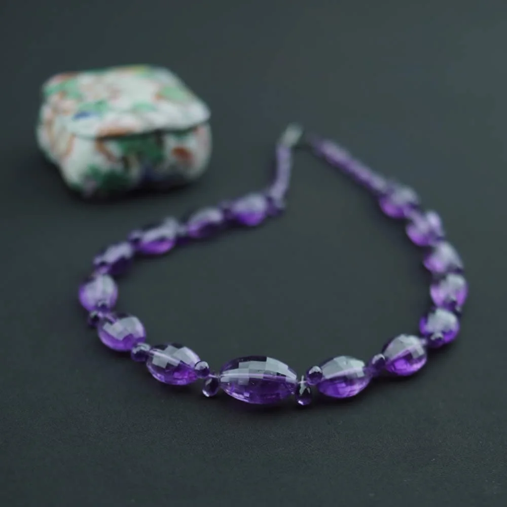 Un collier de pierres fines d’améthyste taillées en forme d’olive et briolette sur une surface noire.