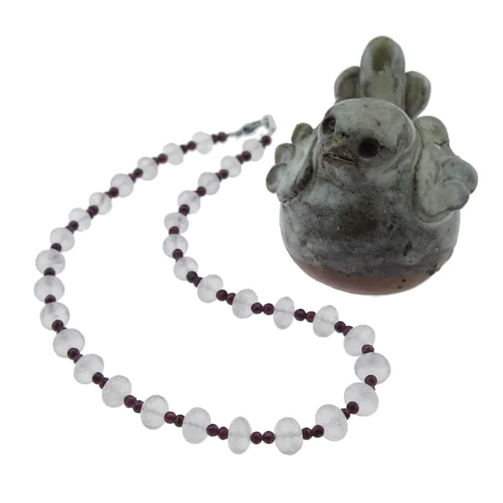 Un Collier léger en quartz rose assorti avec du grenat est posé à côté d'une figurine d'oiseau.