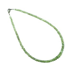 Un collier ras de coup de pierres fines légèrement dégradées et facettées en péridot, posé sur un fond blanc.
